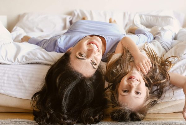 Mother and daughter lying upside down on the edge of a bed, smiling and laughing together